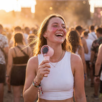 Woman laughing in a festival crowd at golden hour, cooling off with the Frostbite mini turbo fan in soft pink